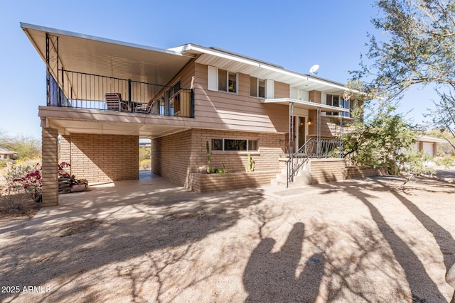 rear view of house featuring driveway, a balcony, a carport, and brick siding