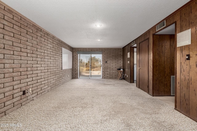 carpeted spare room with visible vents, wood walls, a textured ceiling, and brick wall