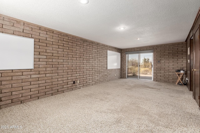 carpeted empty room featuring a textured ceiling and brick wall