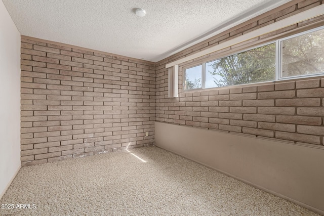 carpeted spare room with brick wall and a textured ceiling