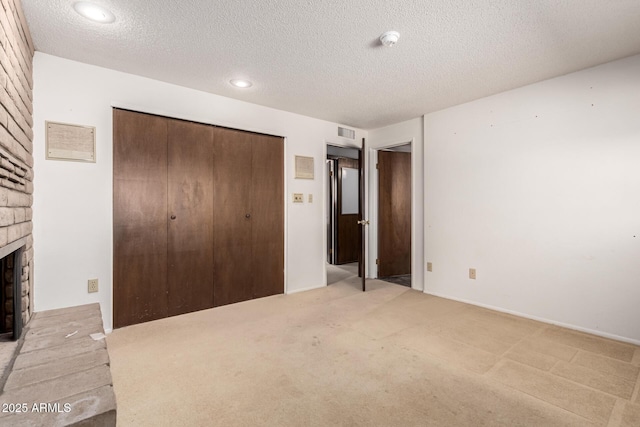 unfurnished bedroom with visible vents, carpet, a textured ceiling, a brick fireplace, and a closet