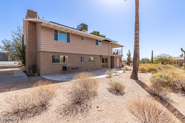 rear view of property featuring a patio, a balcony, a chimney, cooling unit, and brick siding