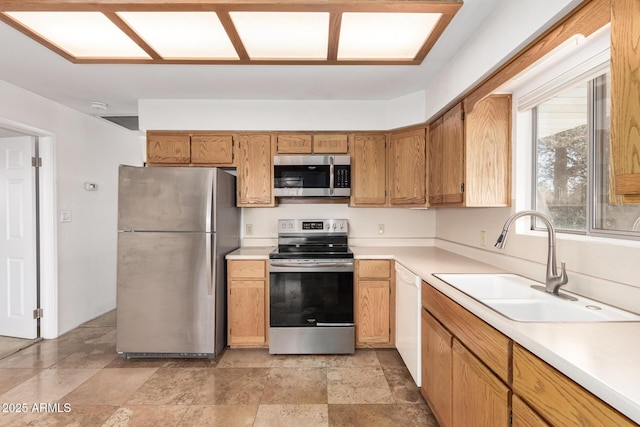 kitchen featuring brown cabinetry, appliances with stainless steel finishes, stone finish flooring, light countertops, and a sink