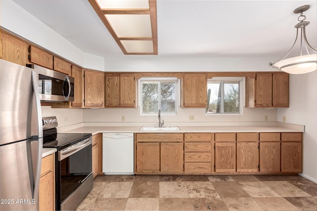 kitchen featuring pendant lighting, brown cabinets, stainless steel appliances, light countertops, and a sink