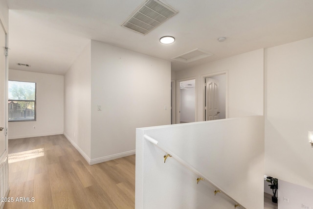 hallway featuring light wood-type flooring, an upstairs landing, visible vents, and attic access