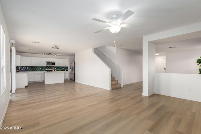 unfurnished living room with baseboards, light wood-style flooring, stairway, and a ceiling fan