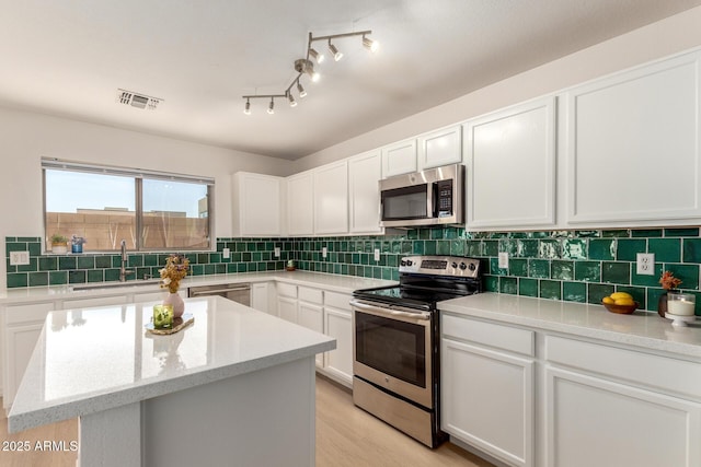 kitchen with stainless steel appliances, a sink, white cabinetry, visible vents, and decorative backsplash