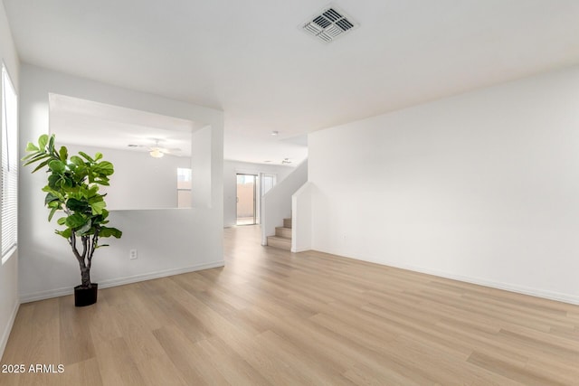 spare room with ceiling fan, light wood-style flooring, visible vents, baseboards, and stairs