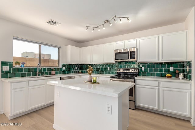 kitchen featuring visible vents, a kitchen island, stainless steel appliances, light wood-type flooring, and a sink