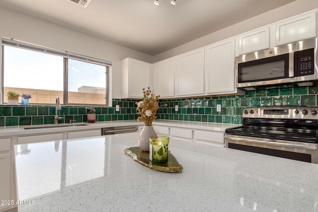 kitchen with stainless steel appliances, white cabinets, a sink, and tasteful backsplash