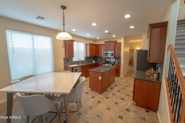 kitchen with pendant lighting, a kitchen island, decorative backsplash, stainless steel appliances, and dark stone countertops