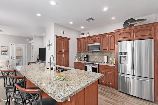 kitchen featuring sink, light stone counters, appliances with stainless steel finishes, tasteful backsplash, and a kitchen bar