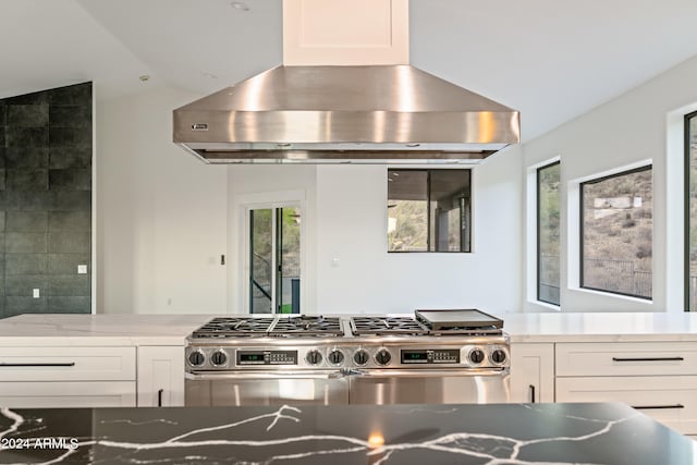 kitchen featuring white cabinets, stainless steel stove, vaulted ceiling, light stone countertops, and island exhaust hood