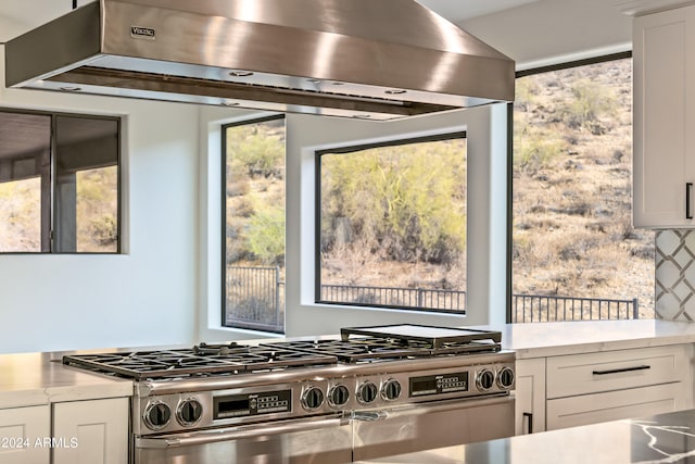 kitchen featuring white cabinetry, a healthy amount of sunlight, stainless steel stove, and wall chimney range hood