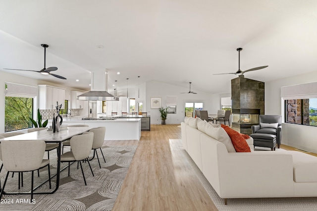 living room featuring lofted ceiling, a tile fireplace, light wood-type flooring, and a healthy amount of sunlight