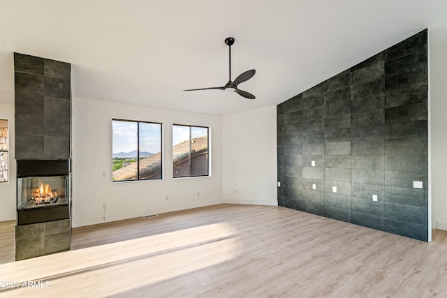 unfurnished room featuring hardwood / wood-style flooring, a tiled fireplace, lofted ceiling, tile walls, and ceiling fan