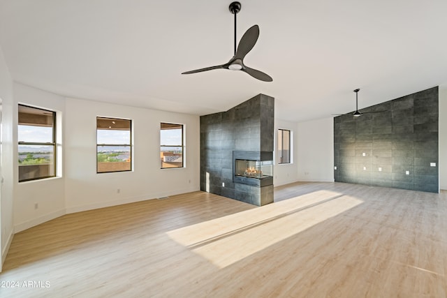 unfurnished living room featuring vaulted ceiling, a tiled fireplace, tile walls, ceiling fan, and light wood-type flooring