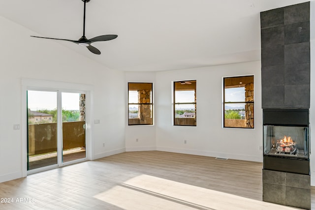 spare room with a tiled fireplace, vaulted ceiling, light hardwood / wood-style flooring, and ceiling fan