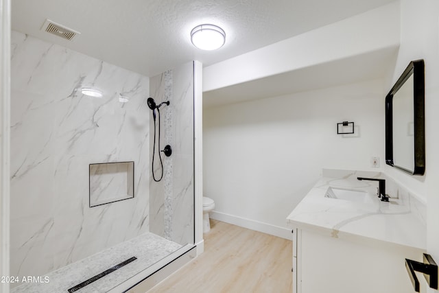 bathroom with hardwood / wood-style floors, toilet, vanity, tiled shower, and a textured ceiling