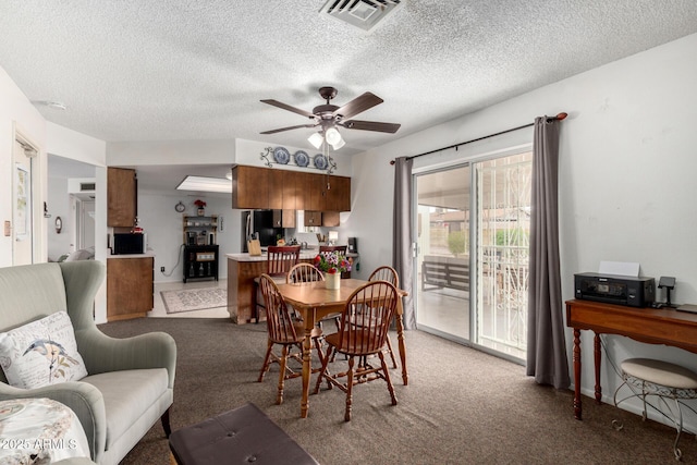 dining room featuring visible vents, light colored carpet, a ceiling fan, and a textured ceiling