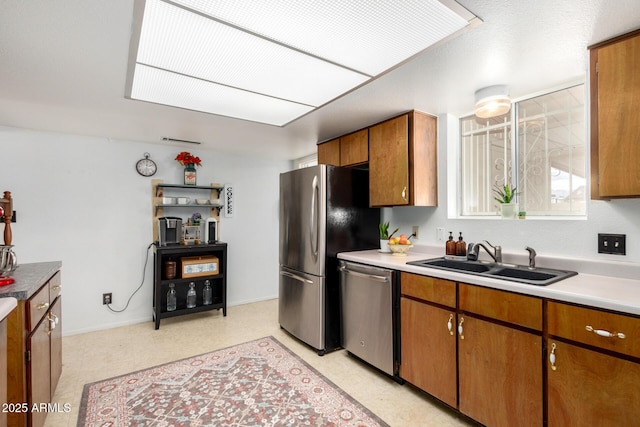 kitchen with a sink, appliances with stainless steel finishes, brown cabinetry, baseboards, and light floors