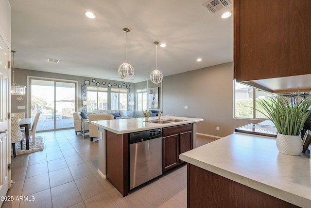 kitchen with light tile patterned floors, an island with sink, decorative light fixtures, stainless steel dishwasher, and sink