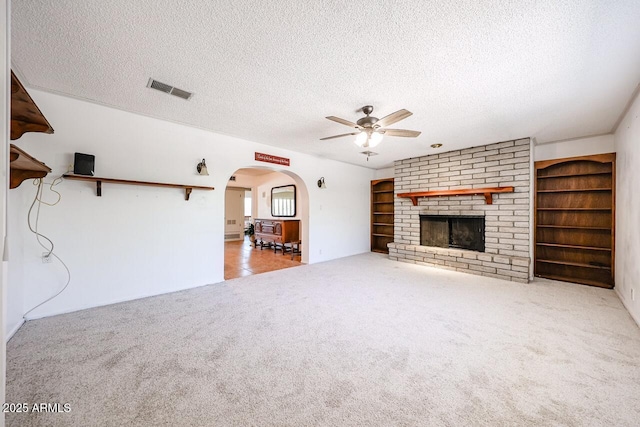 519 N Redondo Dr N, Litchfield Park, AZ 85340 - unfurnished living room with a ceiling fan, carpet floors, a textured ceiling, arched walkways, and a brick fireplace