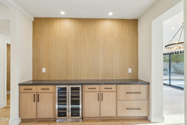 bar with light brown cabinets, light wood-type flooring, and beverage cooler