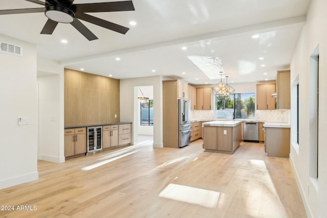 kitchen with appliances with stainless steel finishes, light wood-type flooring, beverage cooler, decorative light fixtures, and a kitchen island