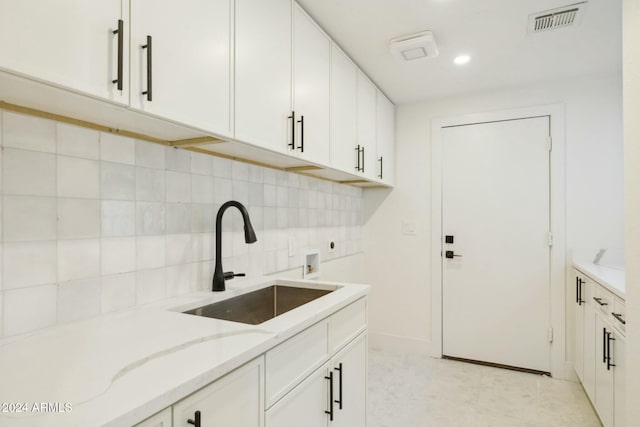 kitchen with light stone counters, white cabinetry, and sink