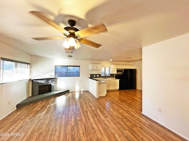 kitchen featuring black fridge, a fireplace, sink, hardwood / wood-style flooring, and white cabinets