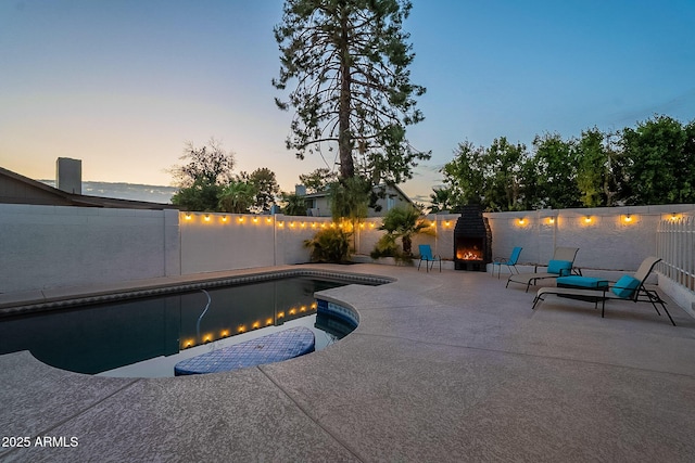 6216 W Poinsettia Dr, Glendale, AZ 85304 - pool at dusk featuring a patio area, a warm lit fireplace, and a fenced backyard