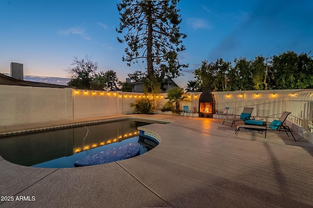 6216 W Poinsettia Dr, Glendale, AZ 85304 - pool at dusk with a lit fireplace, a patio, and a fenced backyard