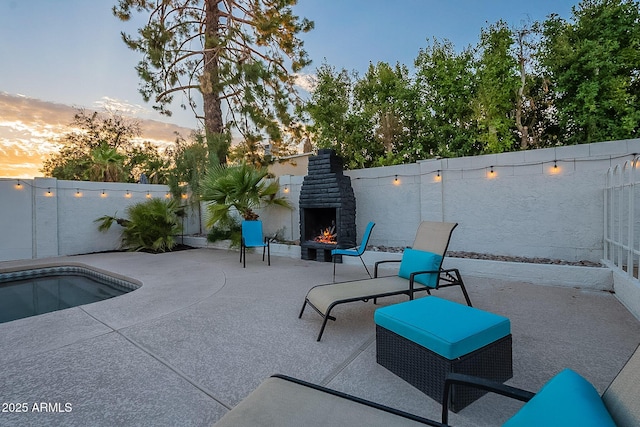 6216 W Poinsettia Dr, Glendale, AZ 85304 - patio terrace at dusk featuring a warm lit fireplace and a fenced backyard