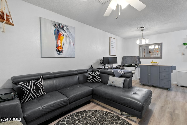 living room featuring ceiling fan with notable chandelier, a textured ceiling, and light wood-type flooring