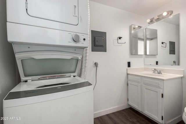 laundry room featuring stacked washer / drying machine, sink, electric panel, and dark wood-type flooring