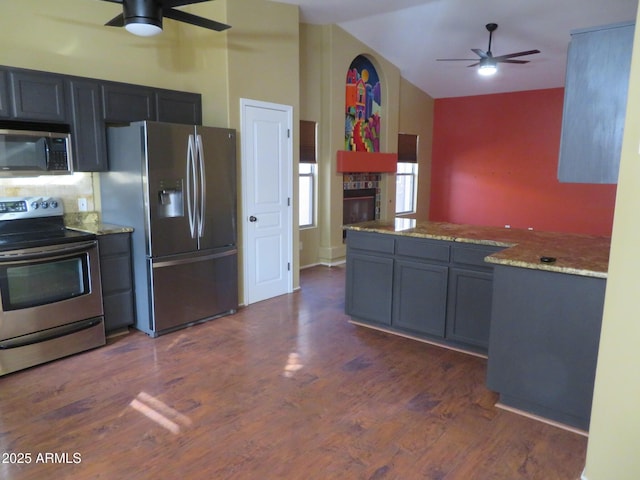 kitchen featuring dark hardwood / wood-style flooring, stainless steel appliances, vaulted ceiling, ceiling fan, and light stone counters