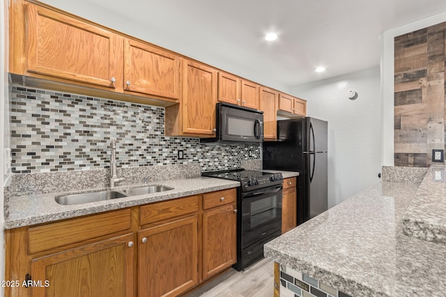 kitchen with a sink, light wood-style floors, backsplash, and black appliances