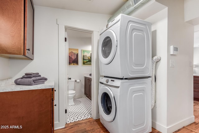 laundry area with baseboards, cabinet space, stacked washing maching and dryer, and light wood-style floors