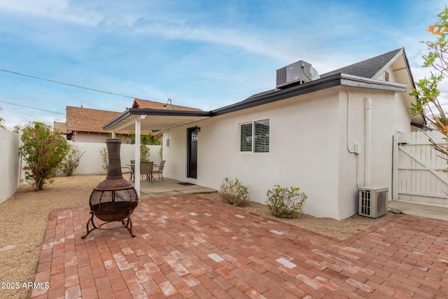 rear view of house with stucco siding, a patio, central AC, a fenced backyard, and a fire pit