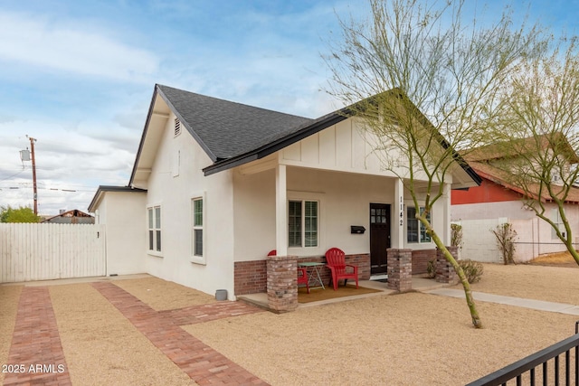 view of front of home featuring stucco siding, fence, brick siding, and a shingled roof