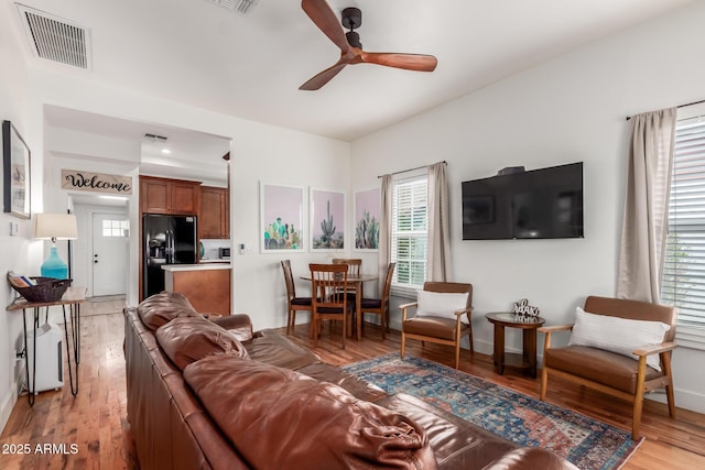 living room featuring visible vents, baseboards, ceiling fan, and light wood finished floors