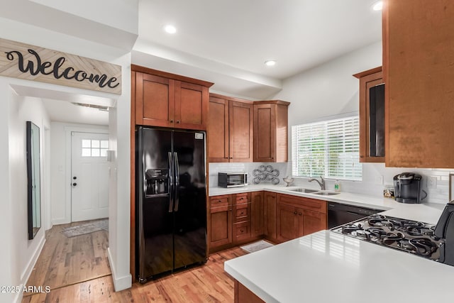 kitchen with a sink, light countertops, dishwasher, light wood-type flooring, and black refrigerator with ice dispenser