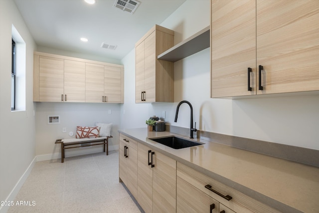 kitchen featuring baseboards, visible vents, light countertops, light brown cabinets, and a sink