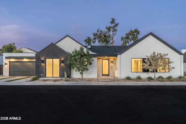 view of front of house featuring driveway, brick siding, an attached garage, and stucco siding