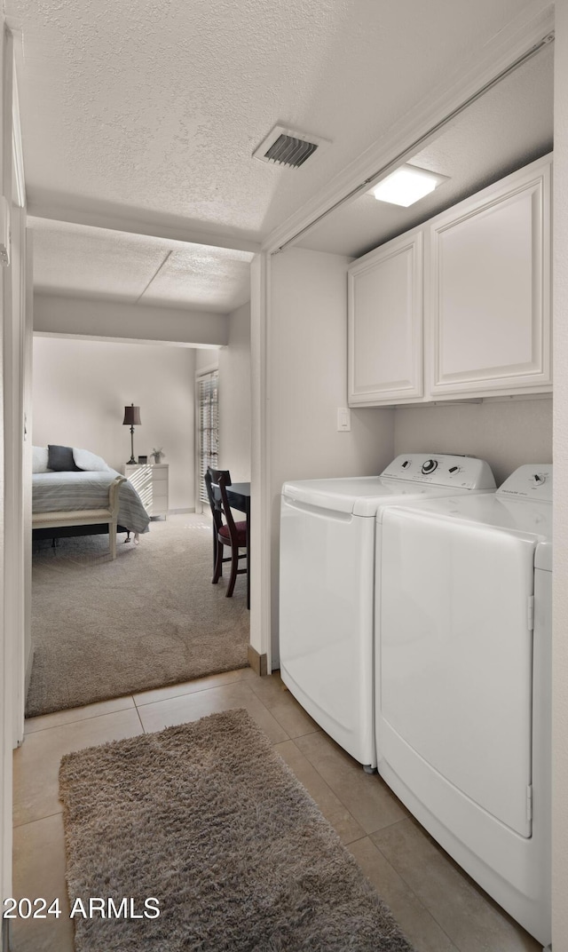 laundry room with a textured ceiling, cabinets, separate washer and dryer, and light carpet