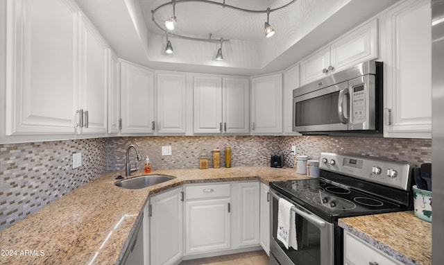 kitchen featuring sink, decorative backsplash, appliances with stainless steel finishes, a tray ceiling, and white cabinetry