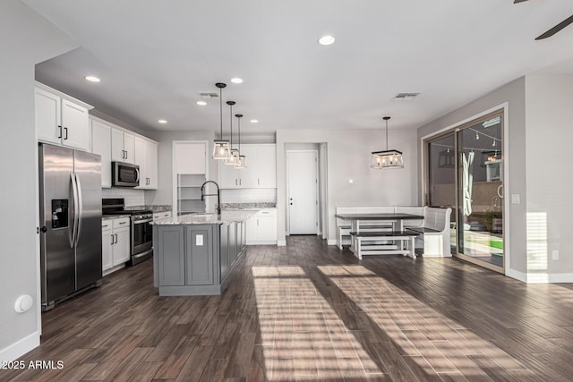 kitchen with pendant lighting, appliances with stainless steel finishes, light stone countertops, white cabinets, and a center island with sink