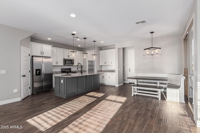 kitchen with pendant lighting, an island with sink, white cabinetry, stainless steel appliances, and light stone countertops