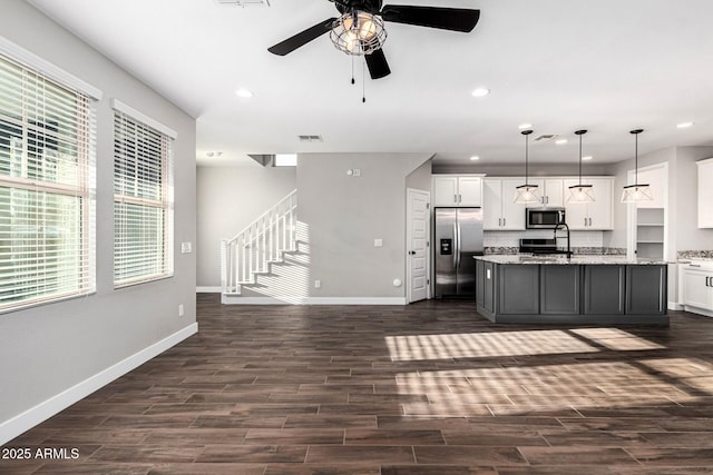 kitchen featuring white cabinets, hanging light fixtures, light stone counters, stainless steel appliances, and a center island with sink